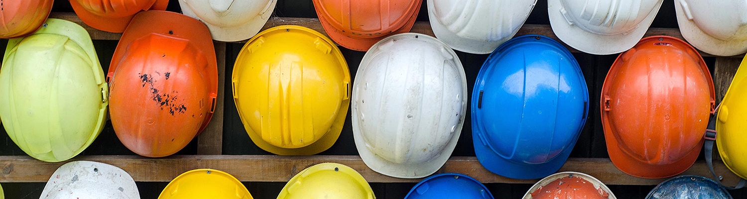 Hard hats in variety of colors hanging on wall.